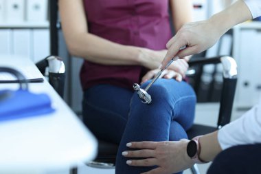 Doktor nörolog klinikte çekiçle hastanın dizine vuruyor.