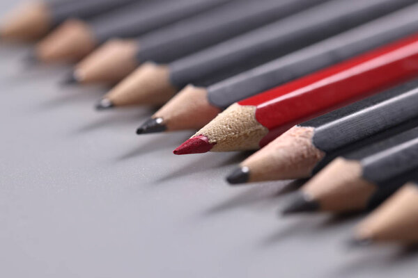 Closeup of one red wooden pencil among many black background