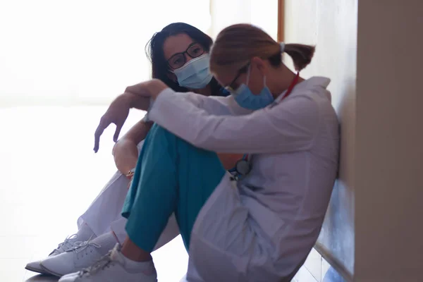 건강을 지키기 위해 마스크를 쓰고 진료소 복도에 앉아 있는 피곤 한 여자 의사들 — 스톡 사진