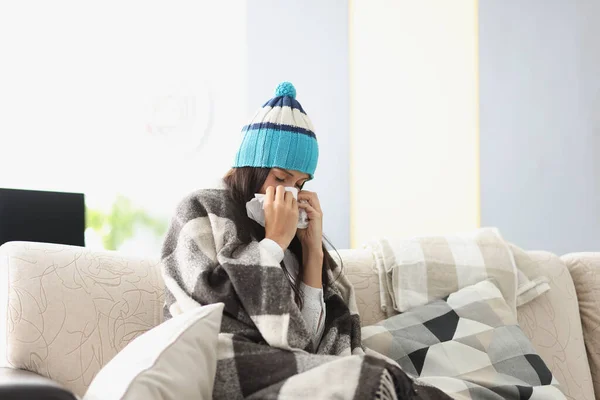 Sjuk kvinna i varm hatt blåser näsan i papper servett hemma — Stockfoto