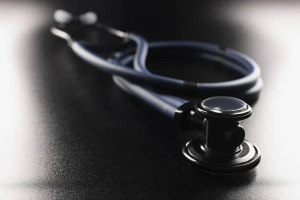 Dark blue stethoscope lying on black background closeup — Stock Photo, Image
