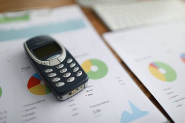 Nokia 3310 cep telefonu, yakın plan grafikli belgeler üzerinde duruyor.