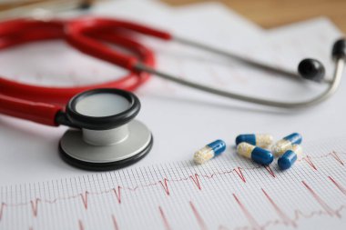 Tıbbi kapsüller ve kırmızı steteskop elektrokardiyogramda yatıyor. Yakın plan.