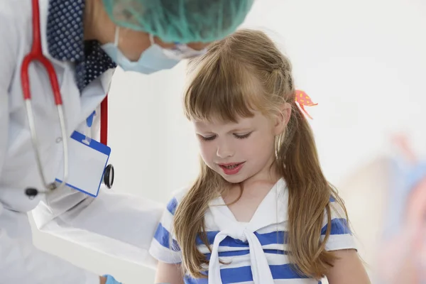 Kinderarzt in medizinischer Schutzmaske spricht mit kleinem Mädchen in Klinik — Stockfoto