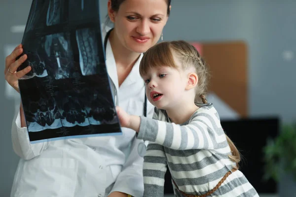 Mujer médico mostrando pequeña niña rayos X en la clínica —  Fotos de Stock