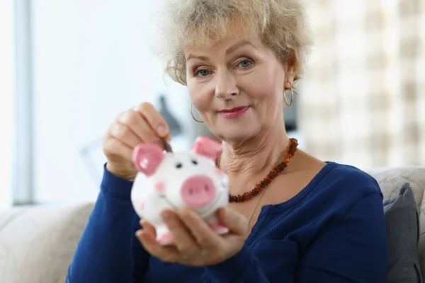 Oudere vrouw zet munt in spaarvarken bank thuis — Stockfoto