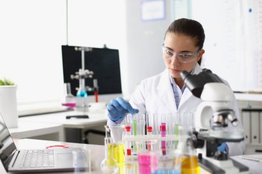 Laboratuvarda mikroskop önünde sıvı ile test tüpü tutan kimyager kadın.
