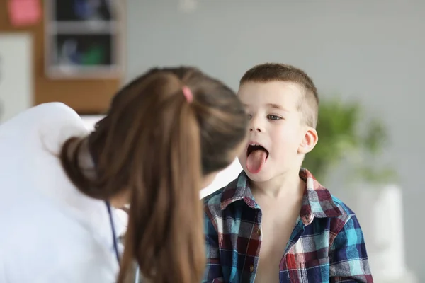 Лікар педіатр вивчає горло маленького хлопчика в клініці — стокове фото