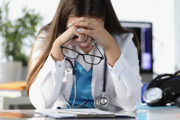 Unavená žena lékař sedí u stolu a drží brýle na klinice — Stock fotografie