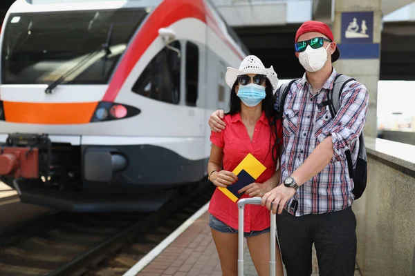 Koruyucu sağlık maskeli genç bir çift ellerinde biletlerle trenin yanında duruyor. — Stok fotoğraf