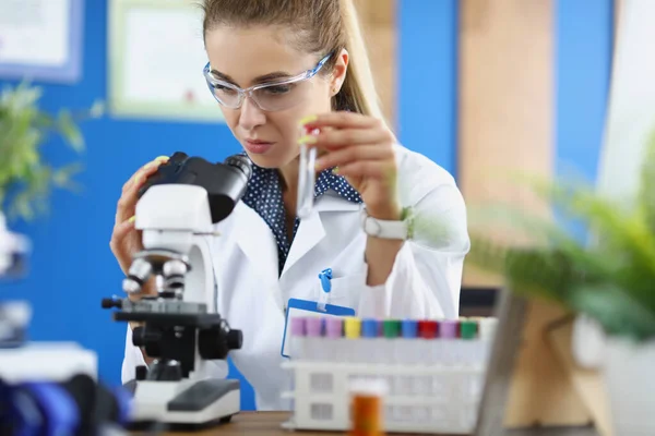 Donna scienziato chimico guardando attraverso il microscopio e tenendo in mano la provetta — Foto Stock