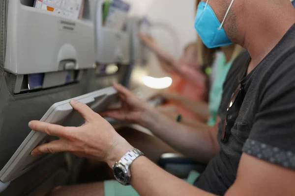 Man i skyddande medicinsk mask lyft bord på flygplan sits närbild — Stockfoto