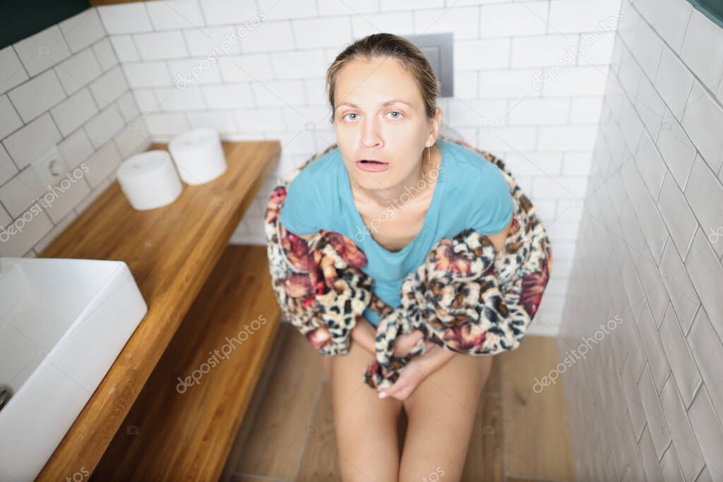 Young woman sitting on toilet and grimacing