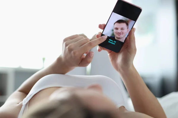 Жінка лежить в ліжку і вибирає чоловіка на сайті знайомств за допомогою мобільного телефону крупним планом — стокове фото
