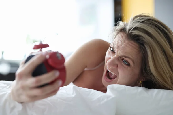 Woman lying in bed with alarm clock in her hands and screaming — Stock Photo, Image
