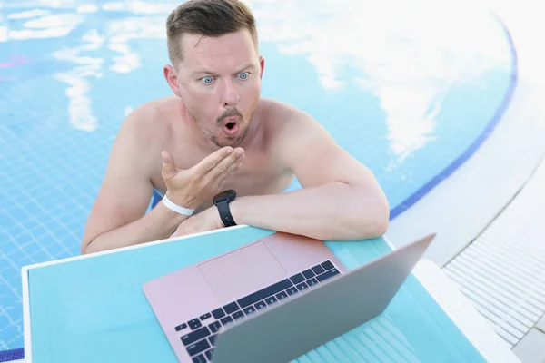 Joven sorprendido en la piscina mira en un ordenador portátil — Foto de Stock