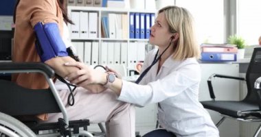 Tekerlekli sandalyedeki engelli kadının tansiyonunu ölçen kadın doktor.
