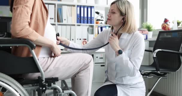 Femme médecin écoute ventre avec stéthoscope pour femme enceinte handicapée en fauteuil roulant film 4k — Video