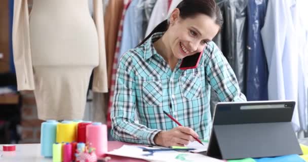 Mujer costurera hablando en el teléfono móvil y escribiendo orden cerca de tableta digital película 4k — Vídeos de Stock