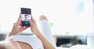 Kadın yatakta uzanıyor ve çöpçatanlık sitesinden cep telefonuyla 4K film çekiyor.