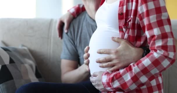 Femme enceinte assise sur les genoux de son mari et caressant le ventre gros plan film 4 k — Video