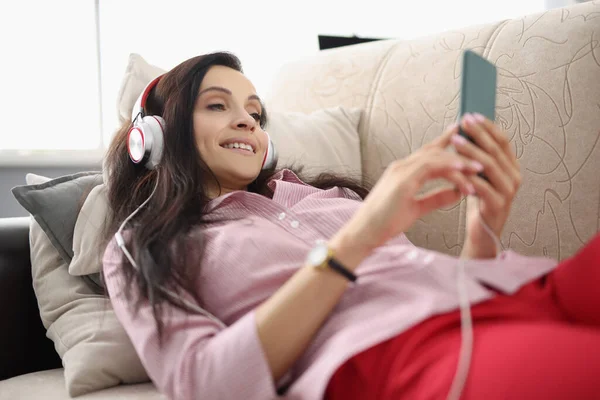 Chilling jovem mulher no sofá com fone de ouvido desgaste smartphone, estudar online — Fotografia de Stock