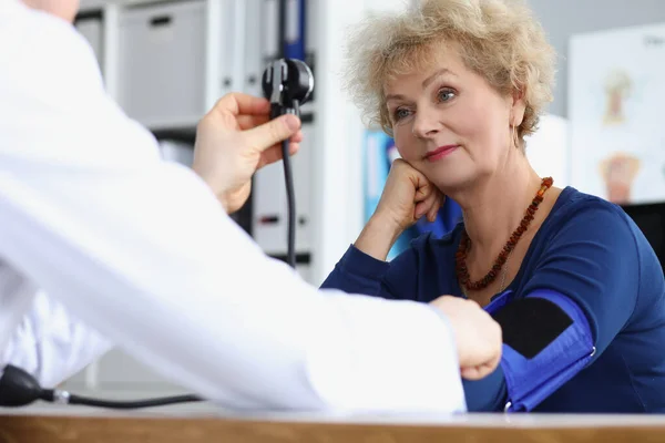 Старшая женщина по назначению, врач измеряет артериальное давление с помощью оборудования — стоковое фото
