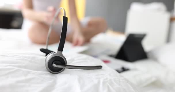 Sluchátka s mikrofonem ležící na bílém polštáři na pozadí ženy pracující na posteli s dokumenty 4k film — Stock video