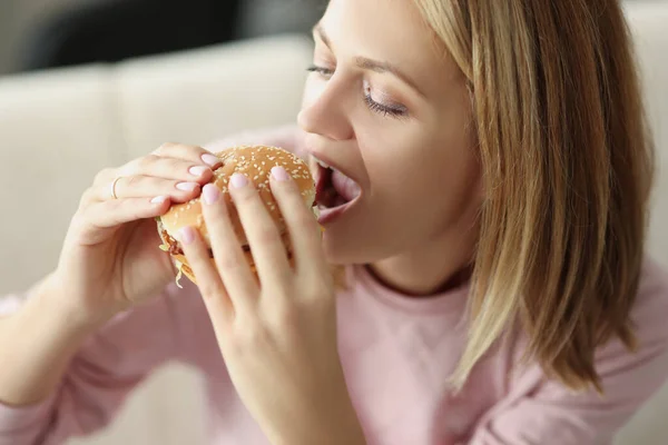Genç sarışın kadın sulu hamburger yiyor, abur cubur yiyor, yağlı öğle yemeği yiyor. — Stok fotoğraf
