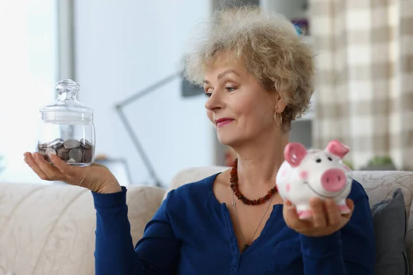 Oudere vrouwelijke hold glazen container met bespaard geld voor pensionering en piggybank — Stockfoto