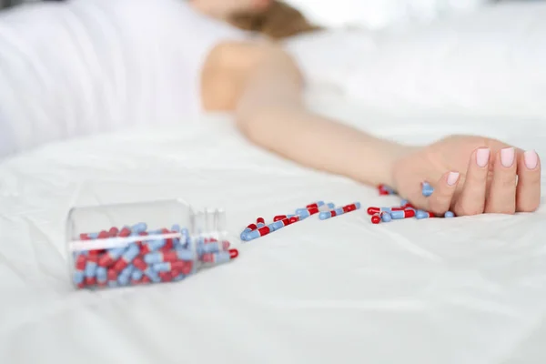 Dead woman lying on bed with scattered medical capsules closeup — Stock Photo, Image