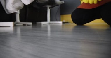 Temizlikçi kadın kanepenin altına bakıyor ve kirli çorap çıkartıyor.