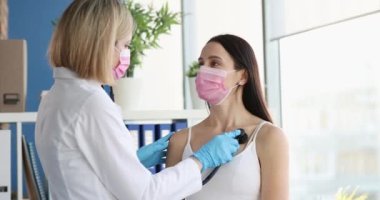 Kadın doktor, tıbbi maskeli steteskopla hastanın akciğerlerini dinliyor. Yakın çekim