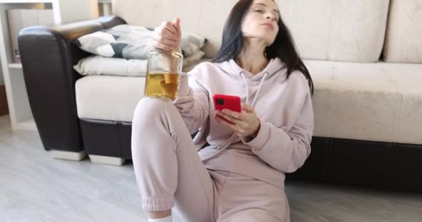 Mulher bêbada senta-se no chão com álcool e escreve sms no smartphone — Vídeo de Stock