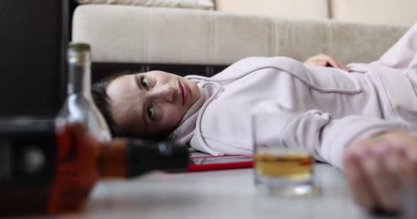 Drunk woman lies on floor with bottles and glass of alcohol closeup — Stock Video