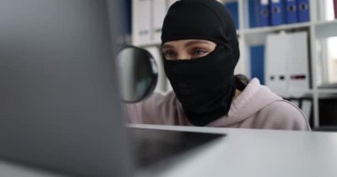 Siyah kar maskeli siber suçlu büyüteç laptop monitöründen bakar.