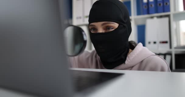 Siyah kar maskeli siber suçlu büyüteç laptop monitöründen bakar. — Stok video