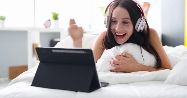 Mujer con auriculares acostada en la cama casa acogedora conversación de videollamada — Vídeos de Stock
