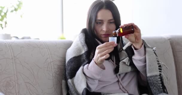 Mujer tosiendo y tomando jarabe para la tos de la botella mientras está sentada en el sofá en casa — Vídeo de stock