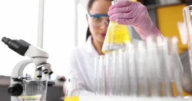 Laboratuvarda elinde sarı sıvı olan bir matara tutan bilim adamı.