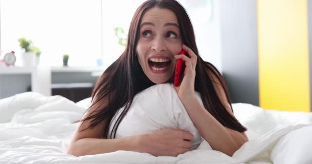 Счастливая молодая женщина разговаривает по телефону, лежа в постели крупным планом — стоковое видео