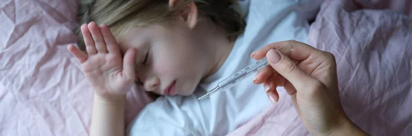 Annem yatakta yatan küçük hasta kızın vücut ısısını ölçer. — Stok fotoğraf