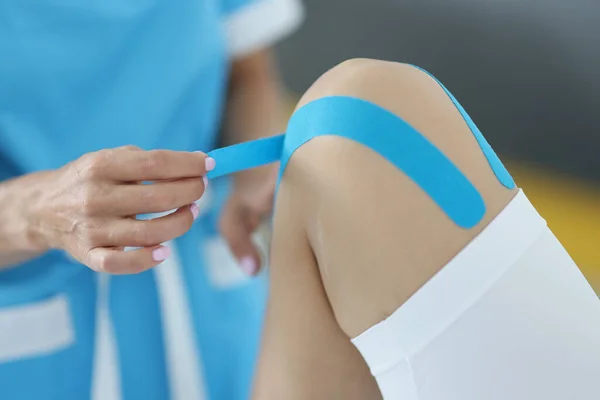 Fyzioterapeut aplikovat kineziologii modrou pásku na koleno klienta — Stock fotografie