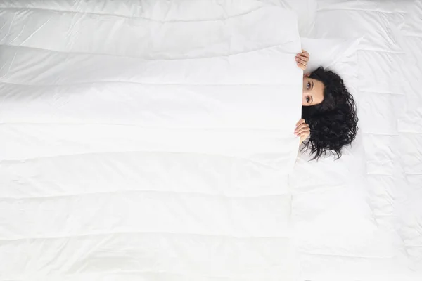 Kadın battaniyeyle kaplanmış beyaz yatağa uzanıyor, sabah dinlenmiş olarak uyanıyor. — Stok fotoğraf