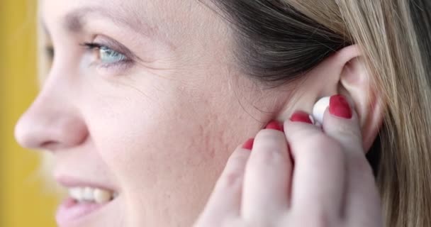 Νεαρή χαμογελαστή γυναίκα που εισάγει λευκά ασύρματα ακουστικά στο αυτί της closeup 4k ταινία — Αρχείο Βίντεο