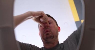 Kapalı burunlu adam tuvalet kapağını açıyor ve lavabo pompalı giysileri çıkarıyor. Alt manzaralı 4K film.