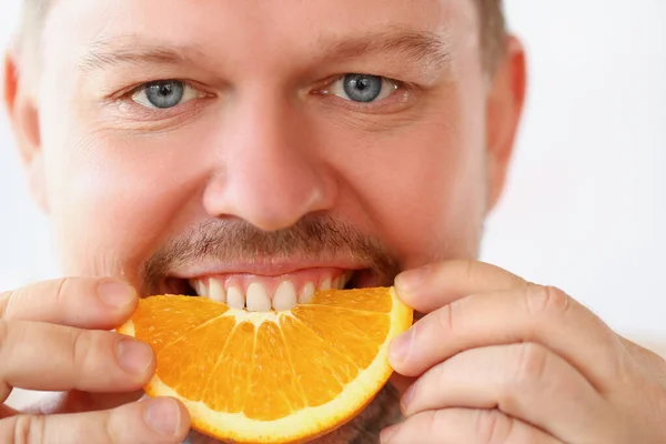 Homem mordida fatia picada de laranja para o café da manhã na cozinha, alimentação saudável, dieta rigorosa — Fotografia de Stock