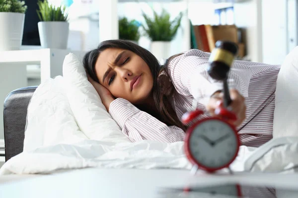 Young woman waking up in bad mood crash alarm with hammer — Stock Photo, Image