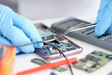 Eldivenli eller cımbızlı akıllı telefon mikroçipini tutuyor.