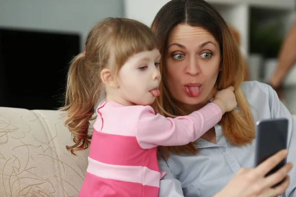 Madre e hija muestran lenguas en la cámara, se divierten tomando selfie en el teléfono inteligente —  Fotos de Stock